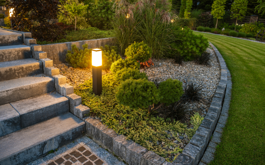 Landscape lighting, next to brick paver steps, showing the ambience of the raised bed and bushes.